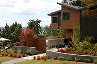 The custom home sits on a slightly sloped lot facing south. Curved concrete walls bracket the entry walk and the fence panel shields the owners from full street exposure. Plant material harmonizes with the house in the tawny brown, orange-red, and purple color scheme. The custom home sits on a slightly sloped lot facing south. Curved concrete walls bracket the entry walk and the fence panel shields the owners from full street exposure. Plant material harmonizes with the house in the tawny brown, orange-red, and purple color scheme.